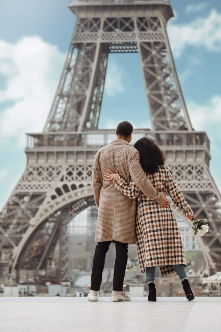 A stylish couple clad in matching houndstooth coats walks hand in hand towards the Eiffel Tower, one of the many romantic activities for couples to do on Valentine's Day in Paris.