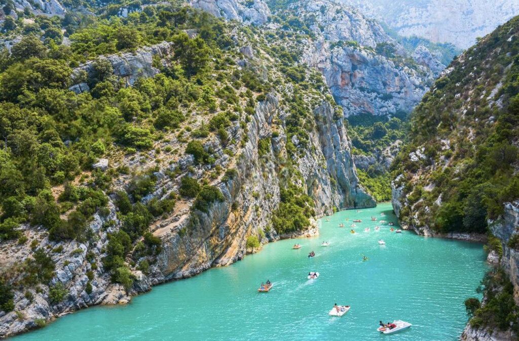 The breathtaking Verdon Gorge with kayakers navigating the turquoise waters amidst steep cliffs and lush greenery, a testament to the natural beauty found in the best cities in the South of France.