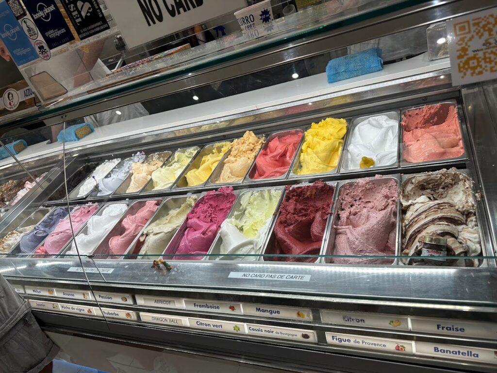 A vibrant display of the best ice cream in Nice at AZZURRO Artisan Glacier, featuring an array of gelato flavors such as apricot, raspberry, mango, and lemon, beautifully presented behind a glass case, inviting customers to choose their favorite scoop.