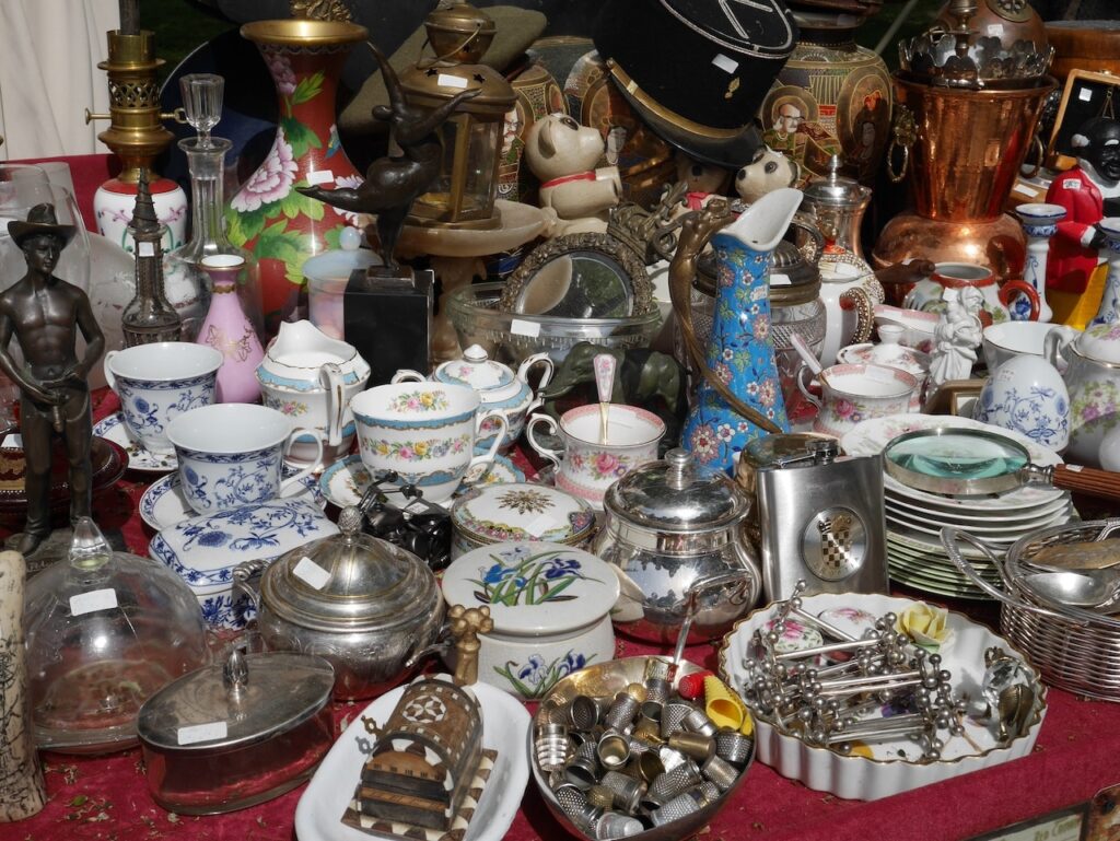 Eclectic assortment of vintage items on display at a flea market in Marseille, including porcelain tea cups, silver teapots, and brass ornaments, a treasure trove for collectors of unique Marseille souvenirs.