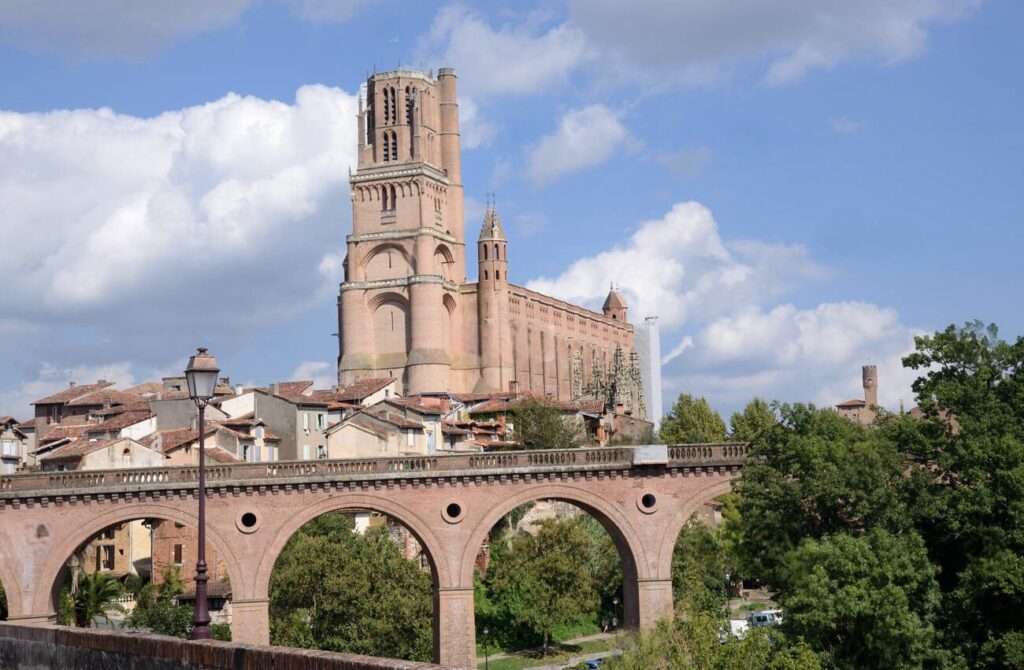 The Sainte-Cécile Cathedral dominates the skyline in Albi, France, featuring prominently alongside the ancient Pont Vieux bridge over the Tarn River, a picturesque embodiment of the best cities in the south of France.