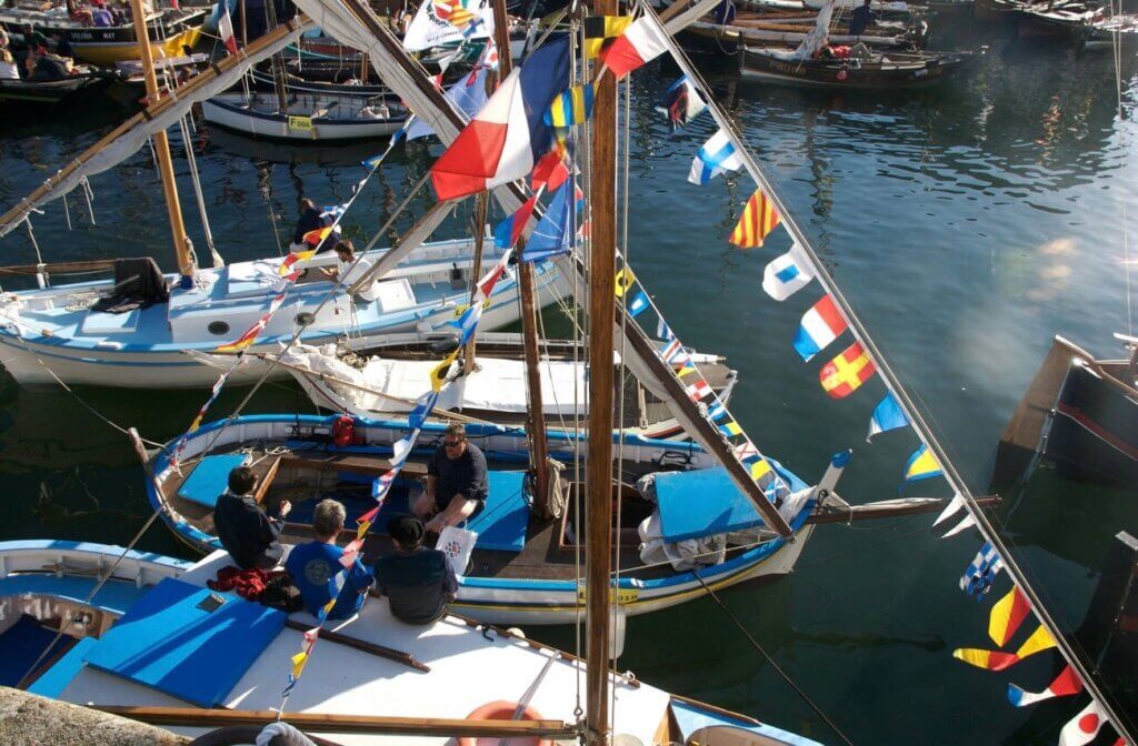 Colorful scene at a Marseille marina with traditional boats adorned with various maritime signal flags, as people gather aboard, reflecting the vibrant maritime culture suitable for Marseille souvenirs.