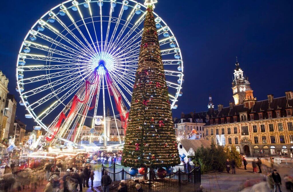 Lille Christmas Market bustling with holiday spirit, featuring a towering Christmas tree and a magnificent Ferris wheel illuminated with white and red lights against the evening sky, with historic buildings providing a picturesque backdrop.