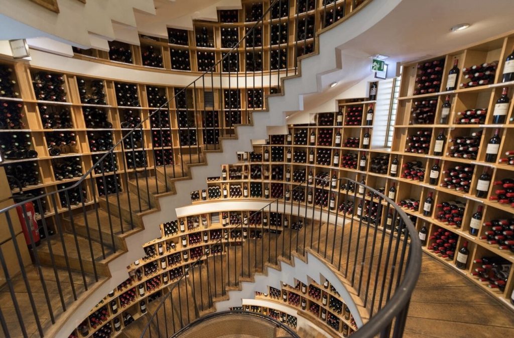 Spiral staircase at L'Intendant, a renowned wine shop in Bordeaux, with walls adorned with an extensive selection of fine wines, inviting connoisseurs to discover local flavors during the winter season.