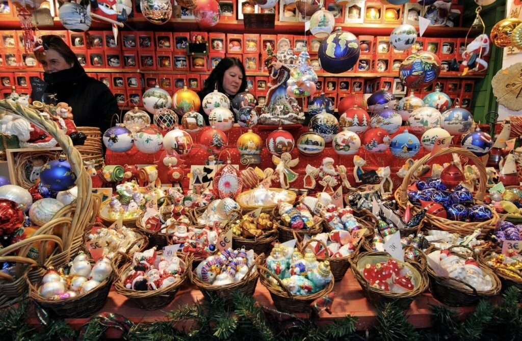 Shoppers browse a colorful selection of handcrafted ornaments at one of the best French Christmas markets, featuring intricately designed baubles in wicker baskets and festive decorations enhancing the holiday spirit.
