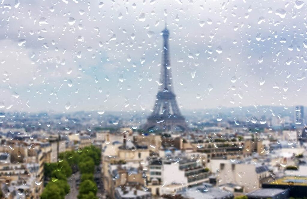 Blurred view of the Eiffel Tower seen through a window with raindrops, highlighting the romantic atmosphere of Paris on a rainy day.