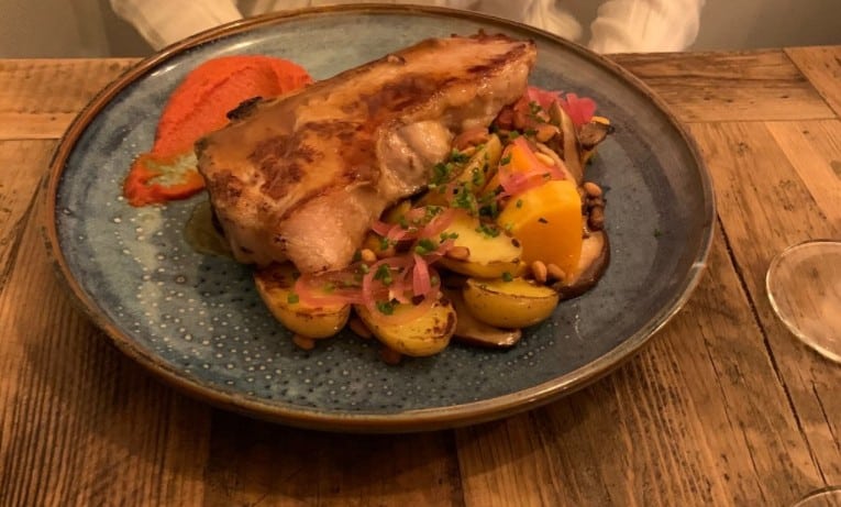 A well-presented plate of roasted chicken thigh served with golden roasted potatoes, garnished with herbs and served on a speckled blue plate at Bistrot Instinct in Paris, capturing the essence of French cuisine.