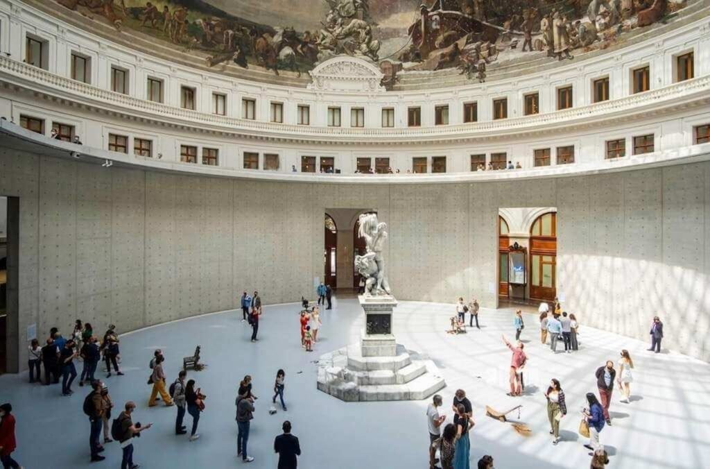 Visitors exploring the grand circular hall of the Bourse de Commerce, featuring a white marble statue at the center, with a striking fresco under the dome and the minimalist design of the surrounding gallery space in Le Marais, Paris.