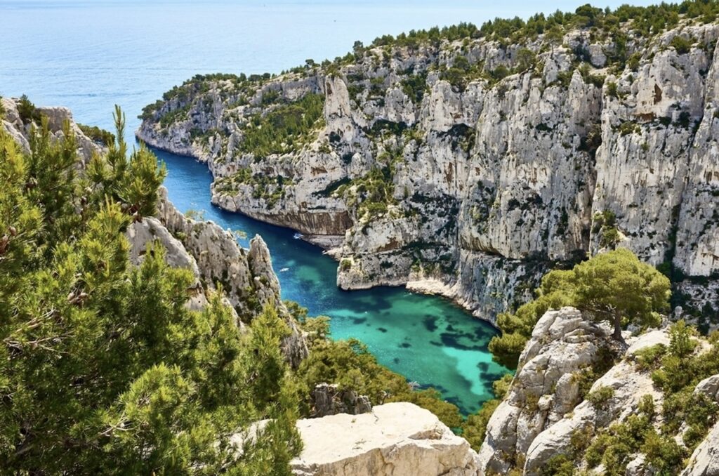 A breathtaking view of the Calanques near Cassis, France, showcasing steep limestone cliffs descending into a secluded cove of azure waters, with lush greenery accentuating the natural beauty of this Mediterranean landscape.