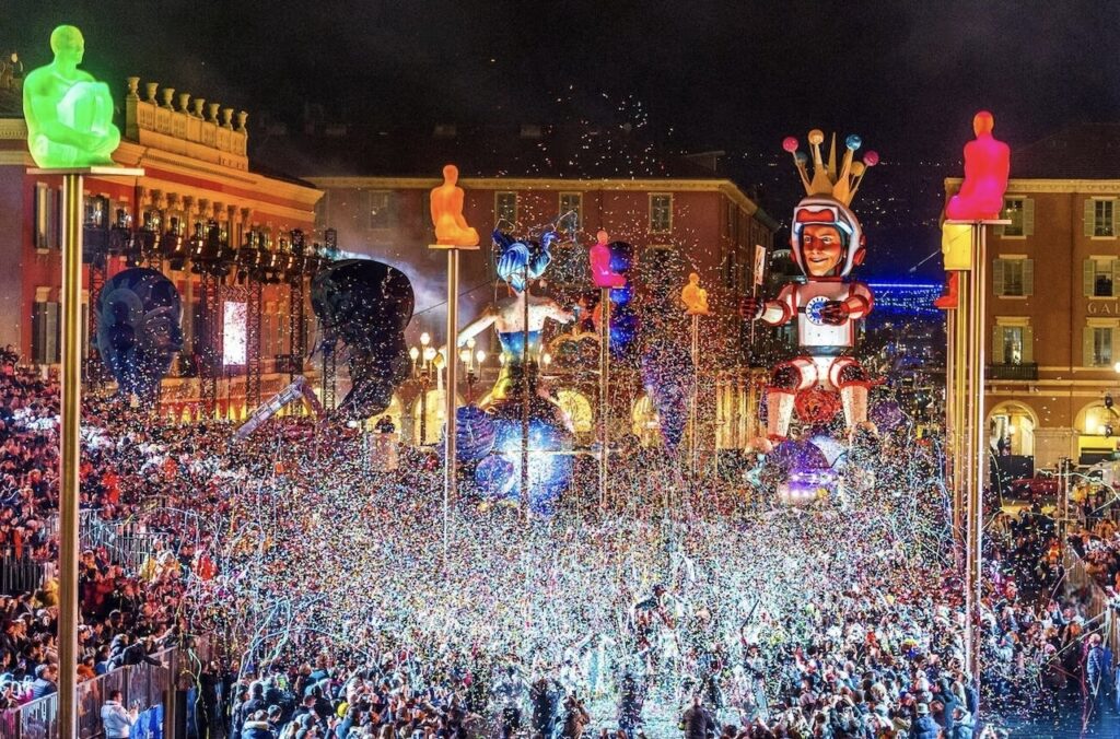 Carnaval de Nice: A spectacular night view of the Carnival of Nice, illuminated with neon lights, showcasing a dense crowd celebrating amidst a shower of confetti, with towering, lit-up figures and a robotic character reigning over the festivities.