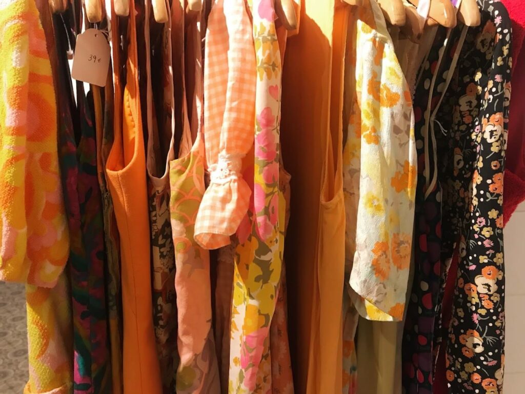 A vibrant collection of vintage clothing on hangers, showcasing a variety of patterns and colors, including floral and geometric designs, with a visible price tag marked '39€' suggesting a sale or boutique setting.
