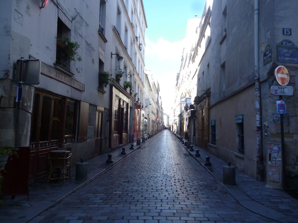 airbnbs in paris: A serene view down a cobblestone street in Paris, lined with traditional buildings and a quiet, empty sidewalk, hinting at the quaint charm of the city's quieter corners.