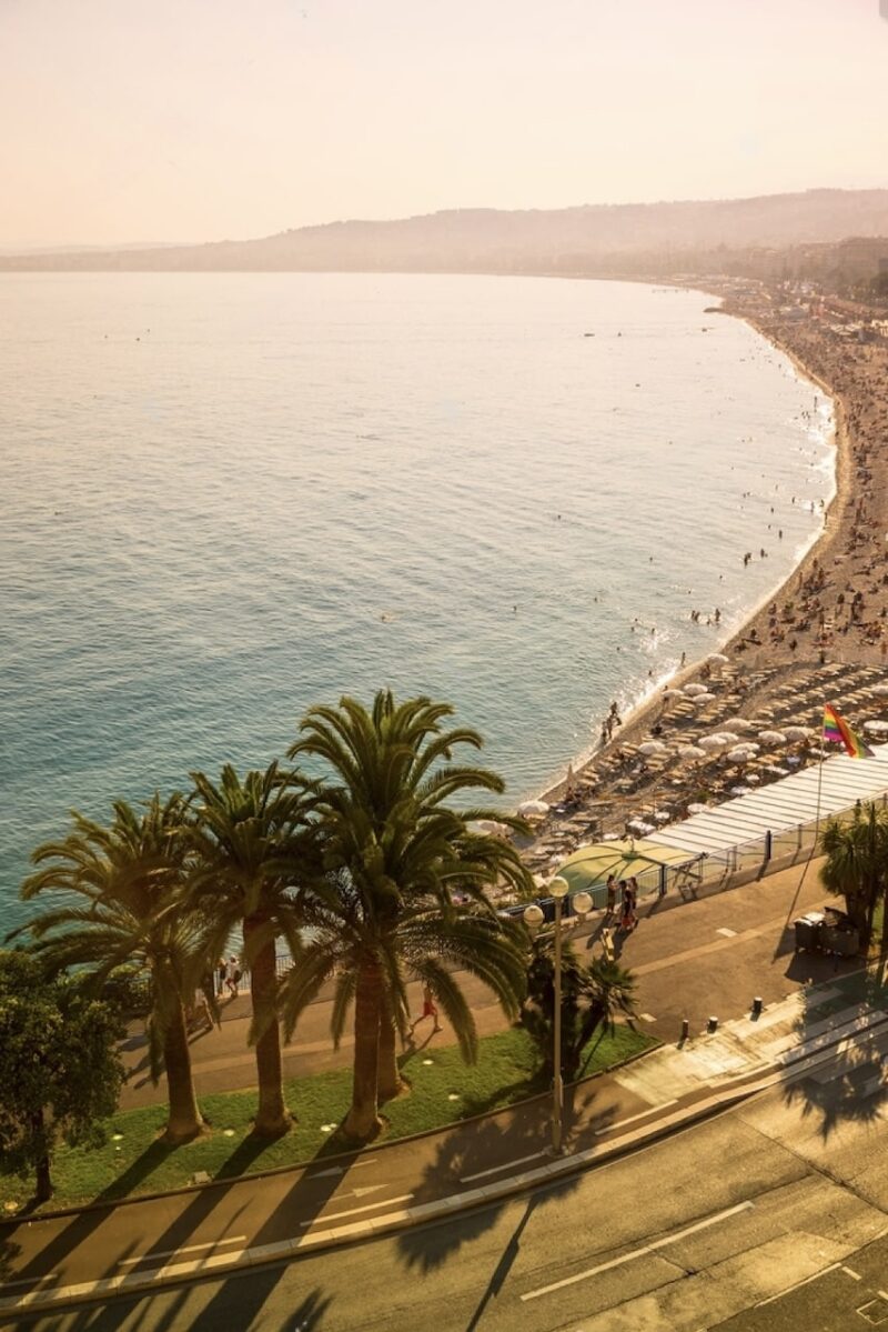 Golden hour view of the Promenade des Anglais in Nice, highlighting the serene Mediterranean Sea and the famous beachfront lined with palm trees, a quintessential scene for any 'Nice in one day' itinerary.
