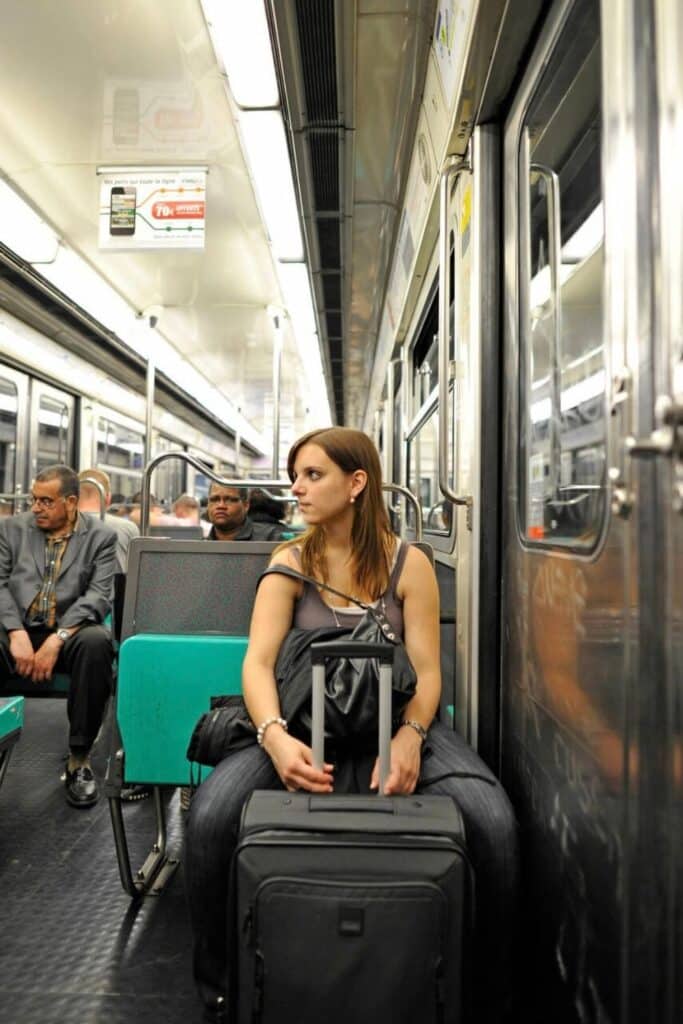 Woman sitting on the Paris Metro with luggage, demonstrating how to use the Metro in Paris when traveling with a suitcase.