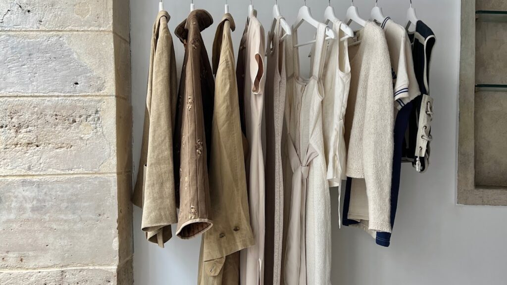 A variety of casual and formal clothing items including jackets, shirts, and sweaters neatly hung on a row of white hangers against a textured stone wall.