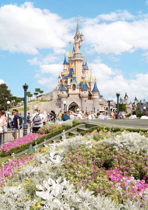Visitors exploring around the iconic Sleeping Beauty Castle amidst vibrant floral arrangements at Disneyland Paris, capturing the essence of 'Disneyland Paris on a Budget' with its fairy tale allure.
