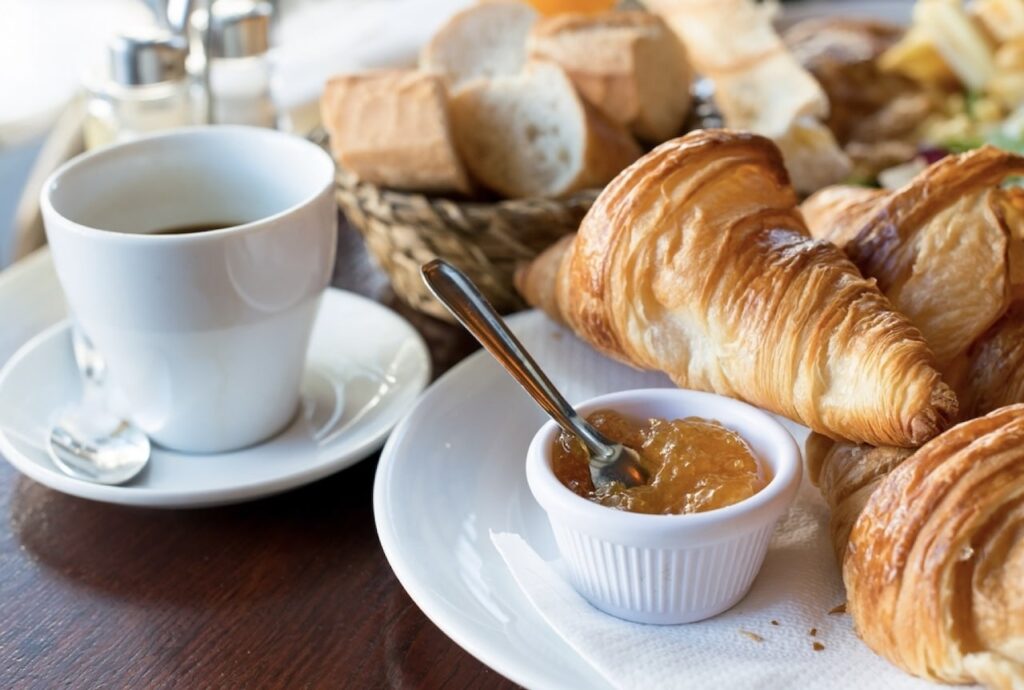 Experience a classic French breakfast on 'food tours in Nice, France' featuring flaky croissants, a cup of hot coffee, and a ramekin of apricot jam, with a background of assorted breads, ideal for a morning start in the French Riviera.
