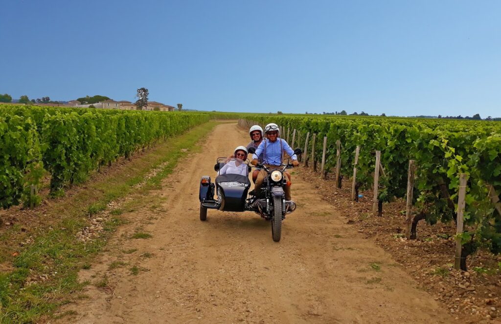 A trio enjoys a sunny ride through lush vineyards on a sidecar motorcycle, an idyllic scene for a motorcycle tour in the famous wine region of Saint-Émilion, France.