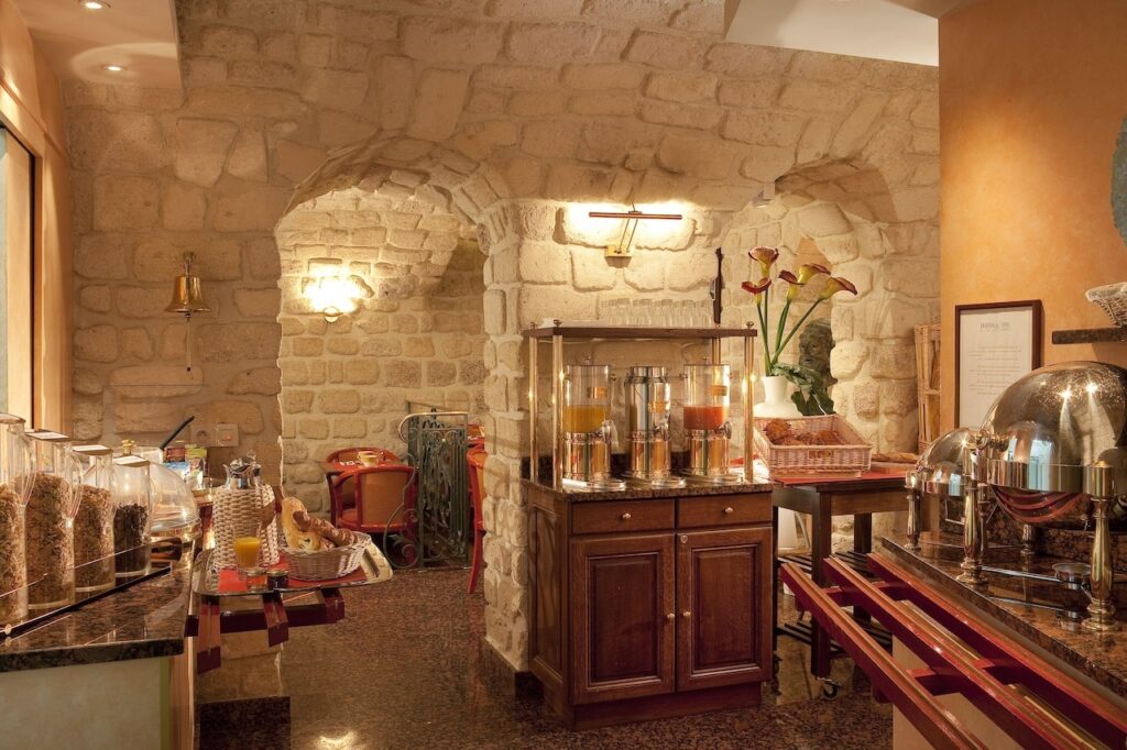 Warm and inviting hotel breakfast nook with rustic stone walls and an array of breakfast items, featuring cereals in glass dispensers, fresh juice, and a selection of pastries, reflecting the charm of hotels in Paris with Eiffel Tower views.