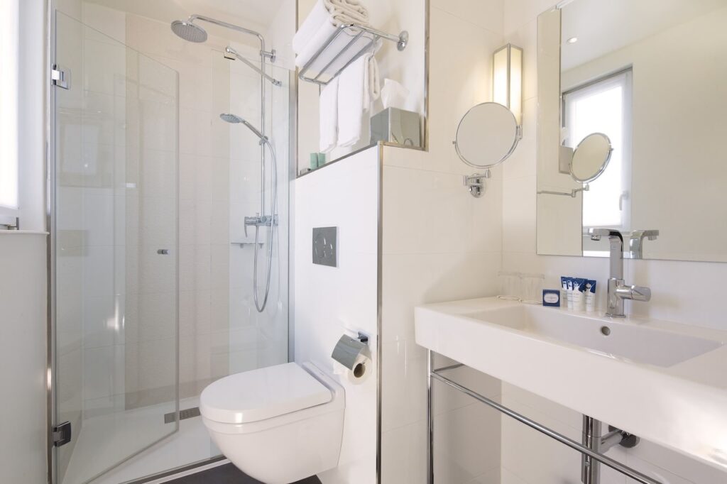 Bright and clean hotel bathroom with a walk-in shower, modern toilet, and a large vanity mirror, complete with fresh towels and complimentary toiletries, suited for guests looking for comfort in hotels in Paris with Eiffel Tower views.