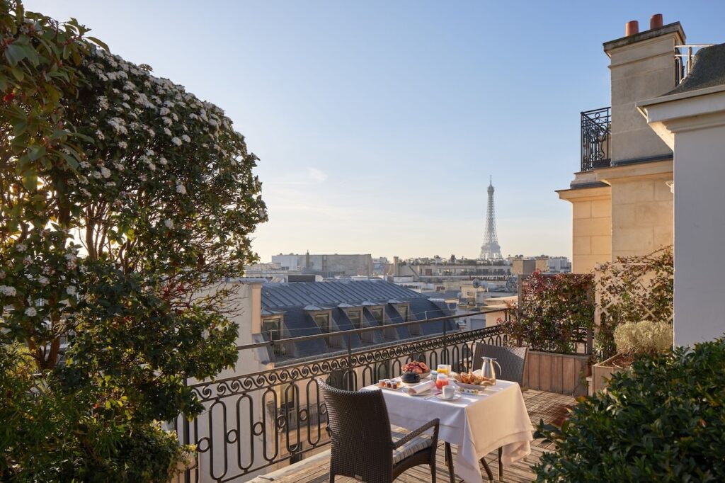 Inviting hotel rooftop terrace set for breakfast with a view of the Eiffel Tower, surrounded by lush flowering plants and the classic Parisian skyline, perfect for a memorable morning at one of the hotels in Paris with Eiffel Tower views.