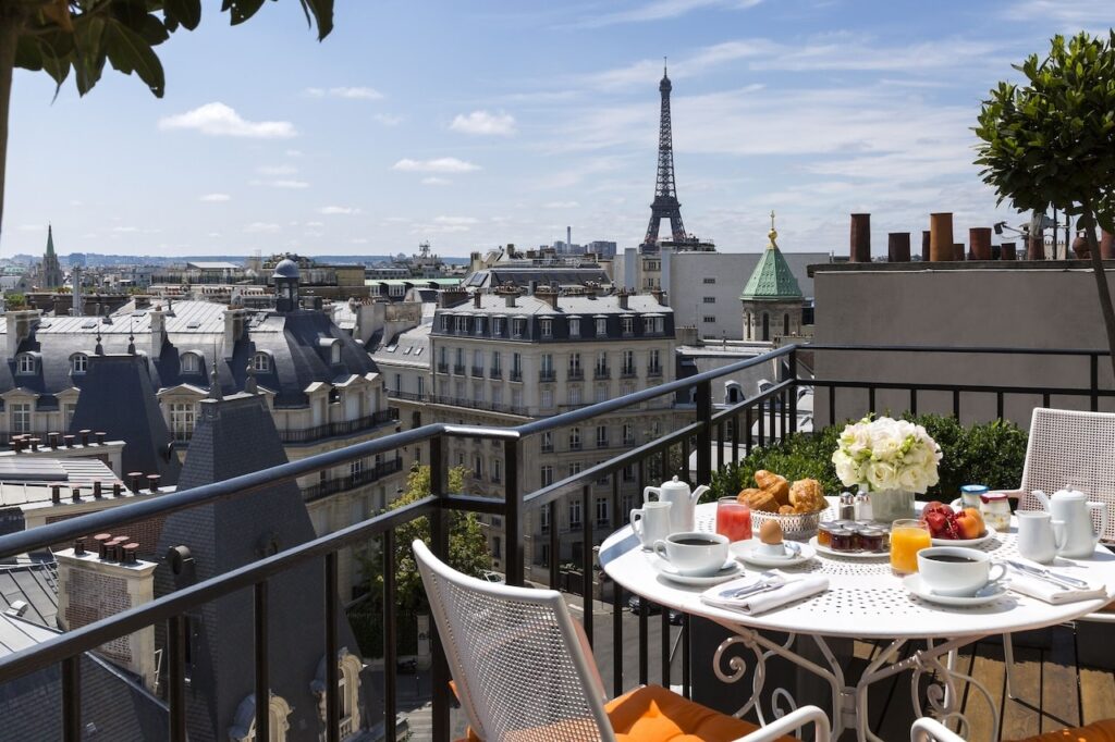 Rooftop breakfast setup on a Paris hotel terrace with a close view of the Eiffel Tower, featuring an elegantly laid table with pastries, fruit, and coffee, framed by the city's charming rooftops, epitomizing the exclusive experience at hotels in Paris with Eiffel Tower views.