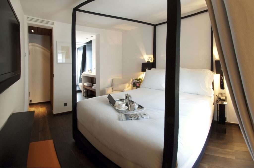 Modern hotel room with a chic four-poster bed, crisp white bedding, and a breakfast tray ready to enjoy, combined with warm lighting and soft drapery that creates a welcoming atmosphere in a Paris hotel with views of the Eiffel Tower.
