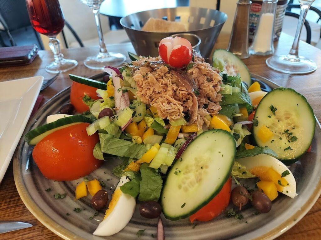 Fresh Niçoise salad, a local specialty on 'food tours in Nice, France', with tuna, eggs, olives, and a medley of crisp vegetables, presented on a plate with a glass of rosé wine, embodying the flavors of the French Riviera.