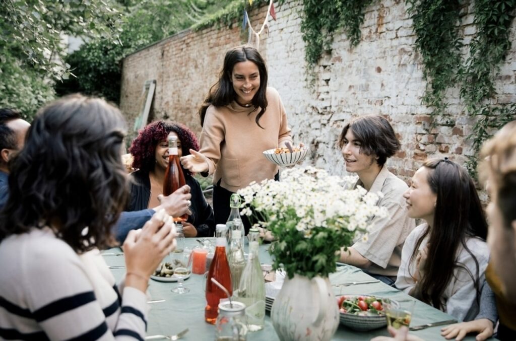 A joyful outdoor dining scene from 'food tours in Nice, France', where a group of friends enjoys organic dishes in a garden setting with a rustic brick wall backdrop, capturing the essence of a communal French meal.