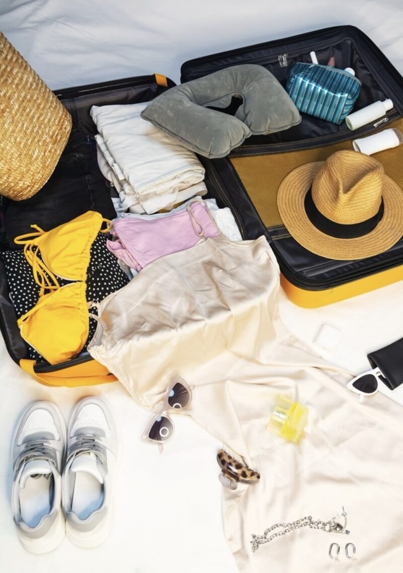 A suitcase filled with travel essentials from a 'Packing List for France', featuring neatly folded clothing, a travel pillow, toiletry bag, straw hat, trendy sunglasses, and comfortable sneakers—everything needed for a fashionable and functional trip in 2024