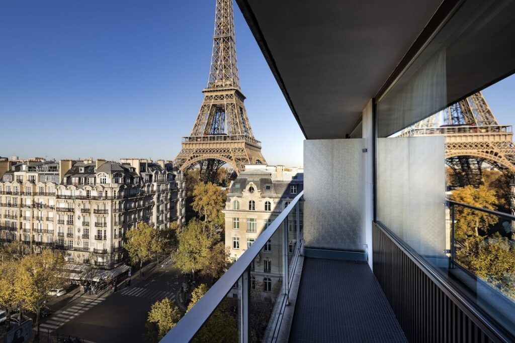 View from a hotel balcony with a dramatic close-up perspective of the Eiffel Tower and the classic Parisian architecture below, captured under a clear blue sky, highlighting the exclusive and stunning views available at hotels in Paris near the Eiffel Tower.