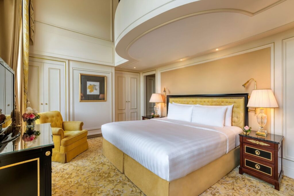 A sumptuous hotel room at the Shangri-La Paris, showcasing a luxurious golden-yellow velvet armchair and bed, with elegant lighting and soft cream tones, offering a blend of classic French decor and modern comfort.