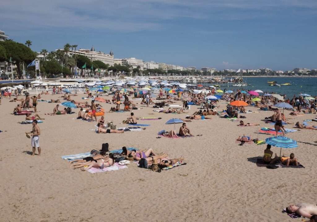A bustling day at the beach in Cannes with sunbathers and colorful umbrellas dotting the sandy shore, capturing the lively beach atmosphere that adds to the charm of the best cities in the South of France.