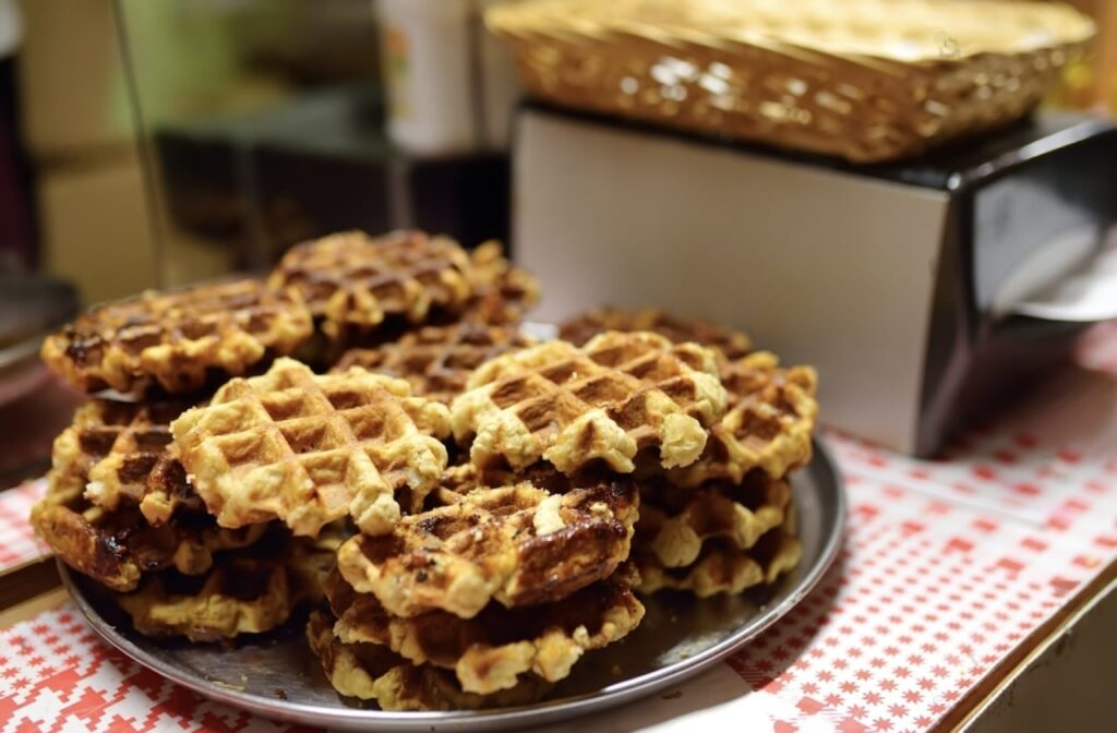 A plate of golden-brown Belgian waffles, with a crisp exterior and soft interior, prominently displayed at a Lille Christmas market stand, evoking a festive holiday treat vibe.