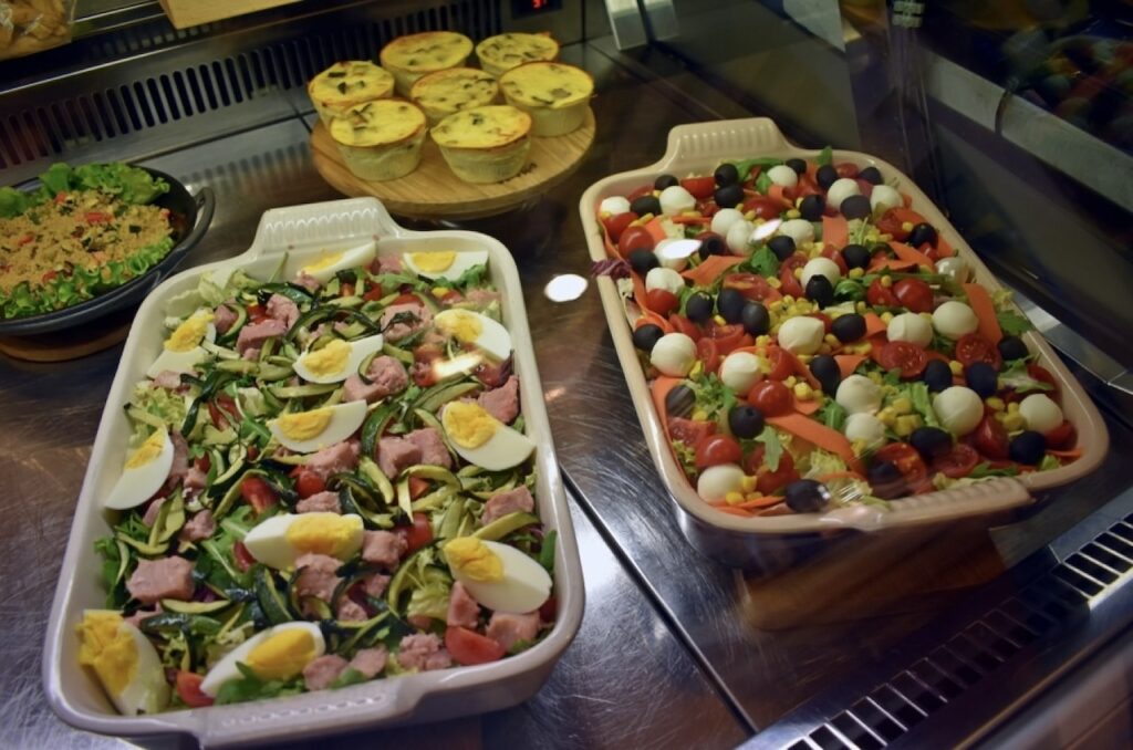 Inside a deli on 'food tours in Nice, France', showcasing a display of colorful salads with ingredients like mixed greens, boiled eggs, and cherry tomatoes, highlighting the fresh produce central to Italian traditional food.