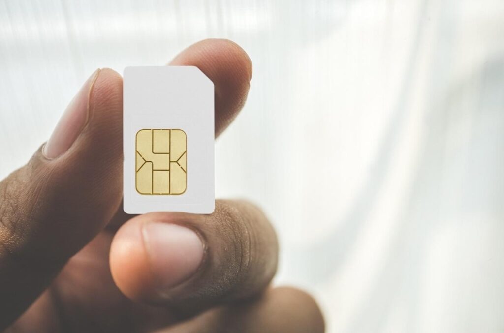 Close-up of a person's hand holding a white SIM card, focusing on the gold circuit part, an essential component for travelers needing connectivity with SIM cards for France.