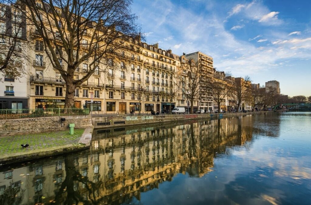 The tranquil Canal Saint-Martin in the 11th arrondissement of Paris, reflecting the elegant Haussmannian buildings in the calm water, a prime example of why this area is often listed among the best arrondissements to stay in Paris for its blend of scenic beauty and cultural vibrance.