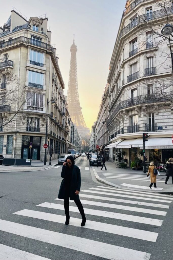 A woman in a chic black outfit poses on a pedestrian crossing on Avenue Rapp, with the iconic Eiffel Tower majestically rising in the background, creating a perfect scene for one of the best Paris Instagram spots.
