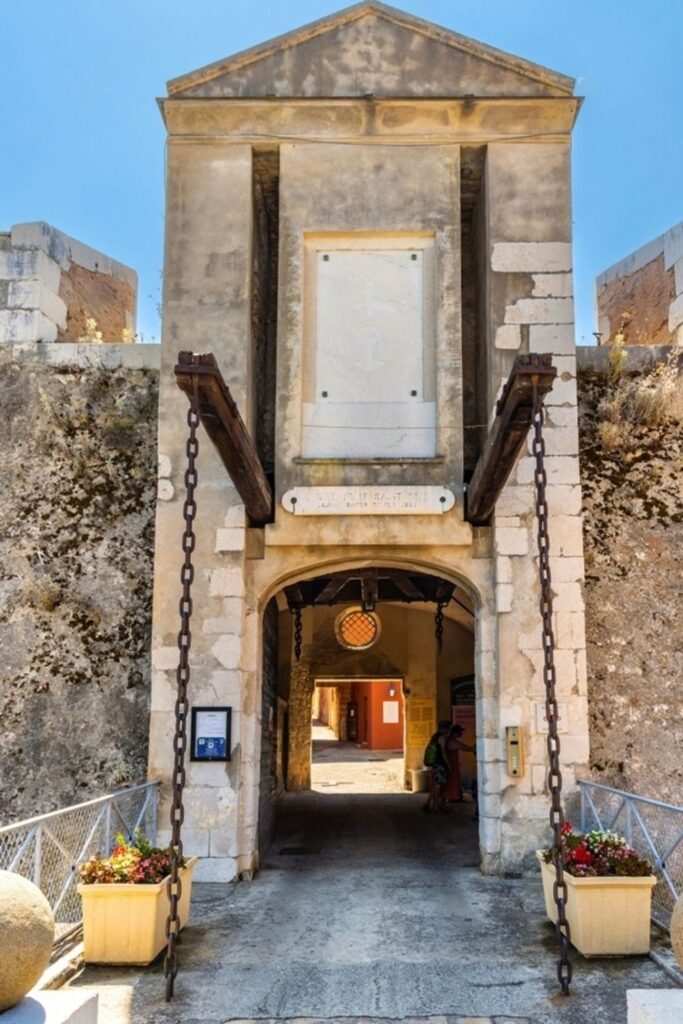 Entrance to the historical Citadel of Villefranche-sur-Mer, showcasing a weathered stone archway flanked by heavy chains and an engraved stone plaque. The passage leads to an inviting courtyard, hinting at a journey into the past, a captivating exploration for visitors looking for things to do in Villefranche-sur-Mer.