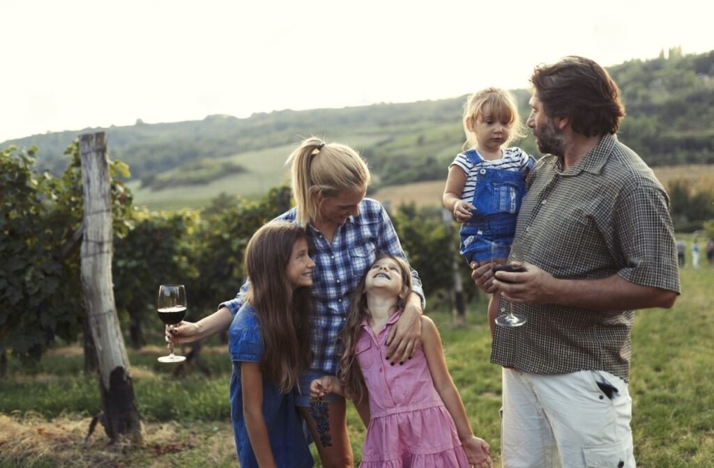 A family enjoys a warm moment amidst the vineyards of Bordeaux, with the mother holding a glass of red wine, reflecting the region's rich wine culture, which is a family-friendly and picturesque activity to add to the list of things to do in Bordeaux.