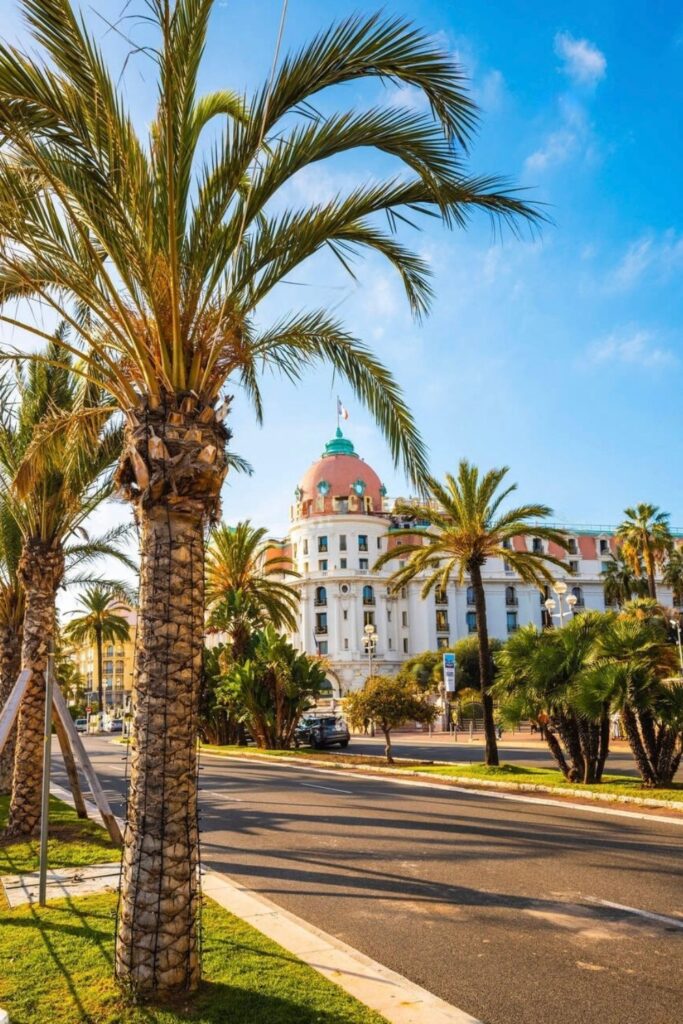 The iconic Hotel Negresco, a symbol of Belle Époque elegance, seen from the Promenade des Anglais in Nice, framed by lush palm trees under a clear blue sky. This landmark hotel is a must-feature destination for any Nice travel guide, representing the luxury and historical grandeur of the French Riviera.