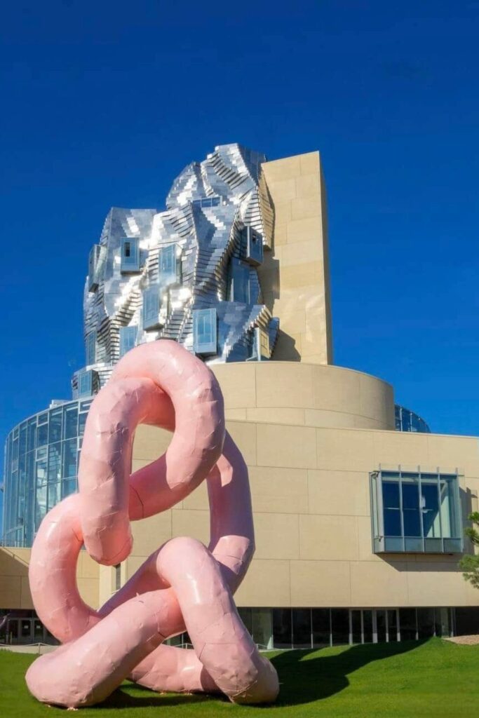 Modern art installation in front of the Luma Arles tower, showcasing a whimsical pink sculpture against the backdrop of the reflective architectural marvel, an engaging sight for visitors looking for the best things to do in Arles.