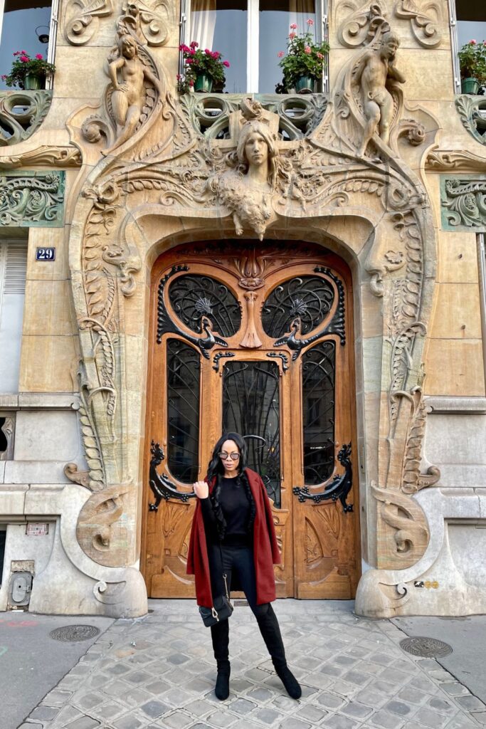 A stylish woman stands confidently in front of the ornate Art Nouveau doorway of the Lavirotte Building at 29 Avenue Rapp, a renowned Paris Instagram spots, showcasing intricate stone carvings and sculptural details.