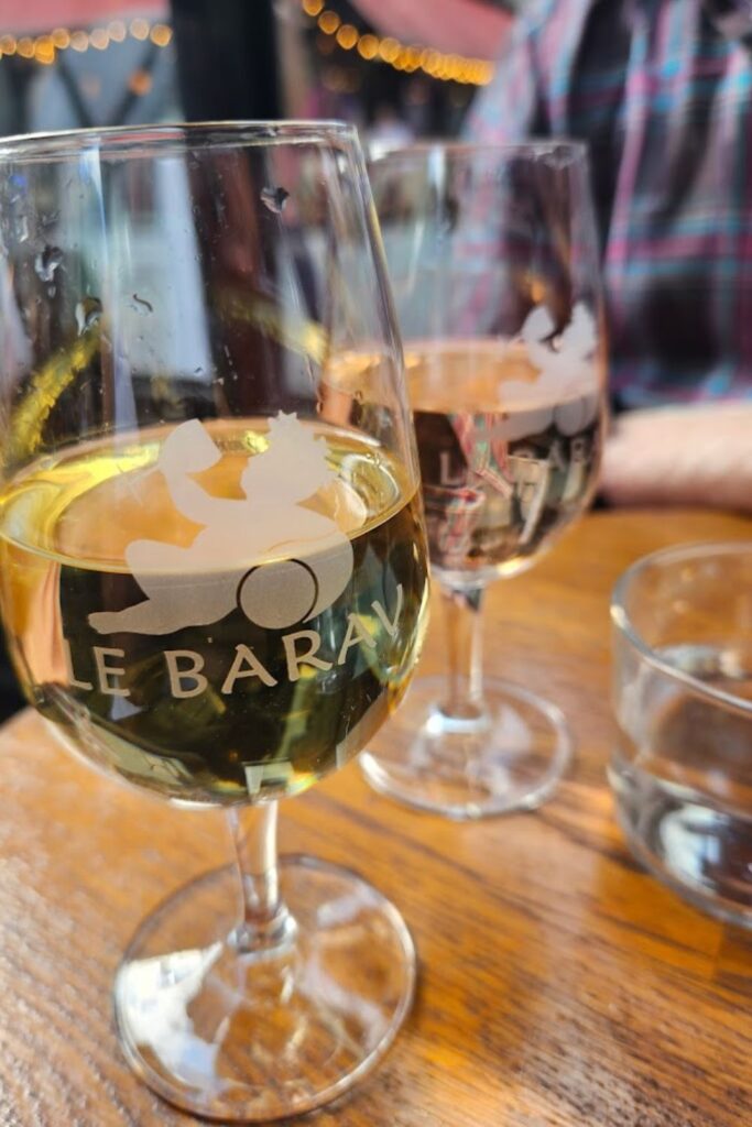 Foreground focus on a glass of white wine with 'Le Barav' etched onto it, alongside another glass of red wine, symbolizing the relaxed yet sophisticated tasting experiences at Paris's finest wine bars.