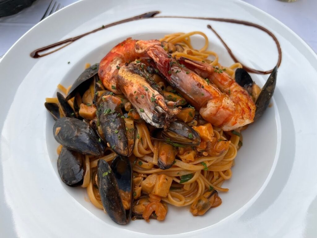A plate of seafood pasta, generously topped with a succulent prawn and fresh mussels in their shells, presented on a white dish—a flavorful glimpse into Marseille's culinary delights experienced in One Day in Marseille.