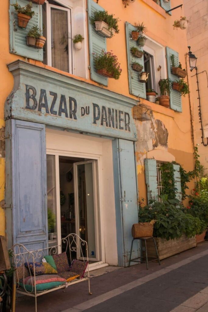 The charming facade of 'Bazar du Panier' in the Le Panier district of Marseille, featuring pastel-colored walls with green shutters and flower boxes, inviting visitors to explore the local shops and culture as a part of their things to do in Marseille.