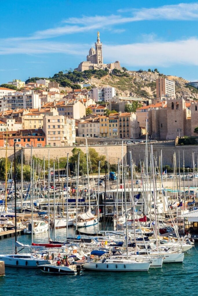 The bustling Old Port of Marseille, brimming with sailboats and yachts, set against a backdrop of terracotta-roofed buildings and the iconic Notre-Dame de la Garde basilica, illustrating a quintessential maritime activity for visitors compiling their list of things to do in Marseille.