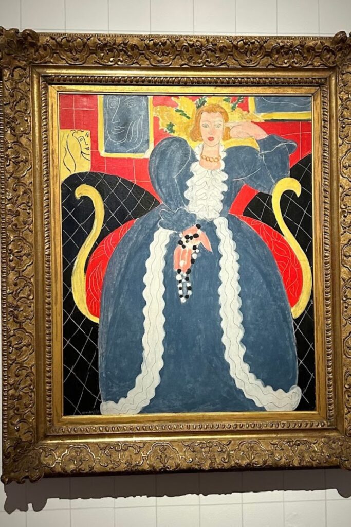 Henri Matisse's bold and colorful painting, featuring a regal female figure adorned with a ruff collar and a striking headdress, displayed in an ornate gold frame. An artistic highlight for any Nice travel guide, this piece from the Matisse Museum showcases the artist's distinctive use of form and color.