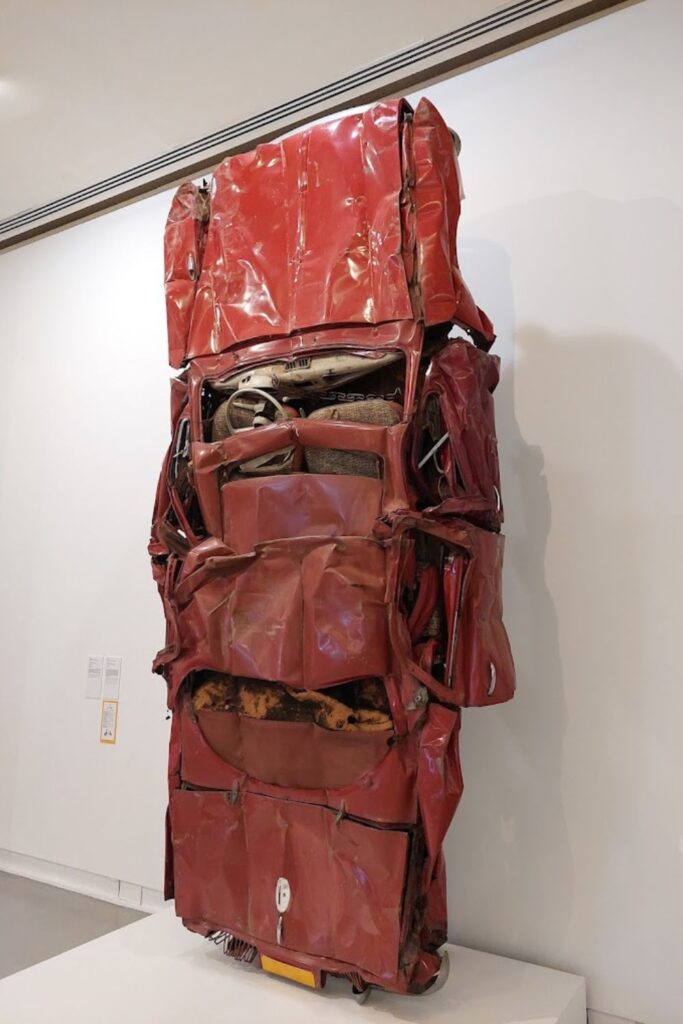 A compelling exhibit at the Modern and Contemporary Art Museum in Nice featuring a vertically compressed red car sculpture. This thought-provoking piece challenges viewers and makes for a striking image in a Nice travel guide, highlighting the city's engagement with contemporary art.
