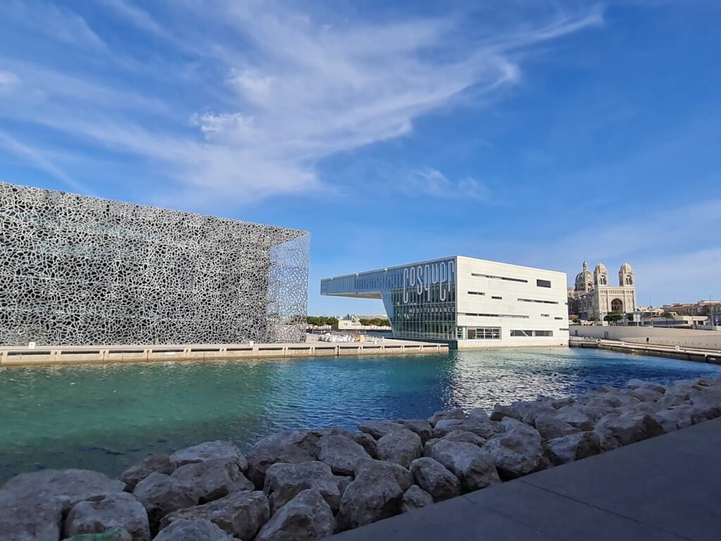 The Museum of European and Mediterranean Civilizations (MuCEM), with its distinctive lacy façade, sits by the sea in Marseille, opposite the grandeur of the Cathedral La Major, epitomizing the fusion of historical and modern architecture experienced during One Day in Marseille.
